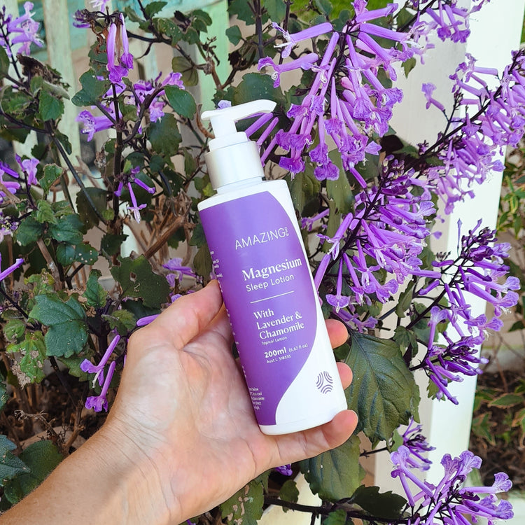 Hand holding a bottle of magnesium sleep lotion with purple flowers in the background