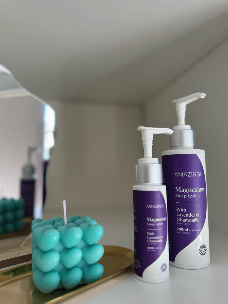 Two bottles of magnesium lotion with pump dispensers on a surface, next to a teal candle.