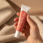 Hand holding a tube of Magnesium 'Ugly Bits Stick' blemish correction on a beige background